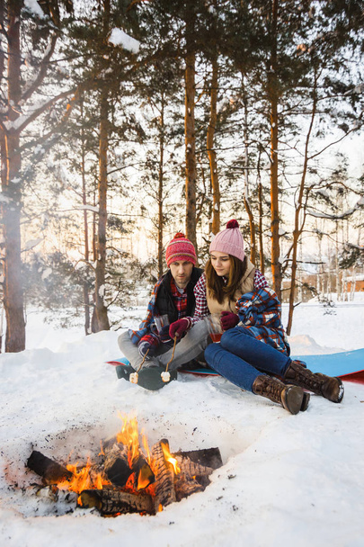 young couple fry marshmallows on a fire in winter in a forest under a rug - Foto, Imagem