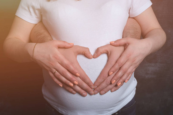 Батьки роблять серце на животі вагітної матері на темному тлі, тонізуючи
 - Фото, зображення