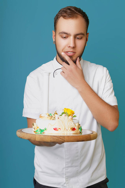 young male confectioner in a tunic with cake in the studio - Фото, изображение