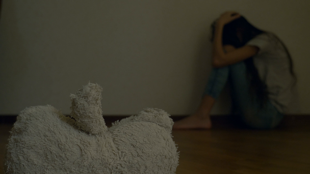 egy kétségbeesett gyermek depresszió a fal a szobájában ül, megpróbálja öngyilkossági kísérlet. mellette van egy elhagyott játék. 4k, lassú mozgás. - Felvétel, videó