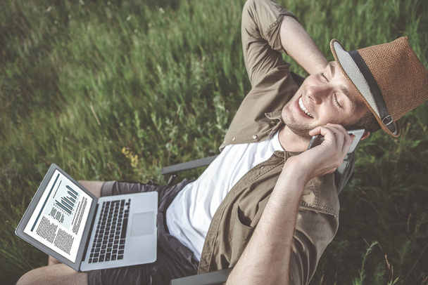 Delighted man is resting on field while having phone conversation - Photo, Image
