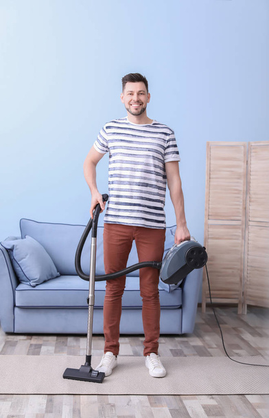 Mature man hoovering carpet with vacuum cleaner in living room - Foto, Bild