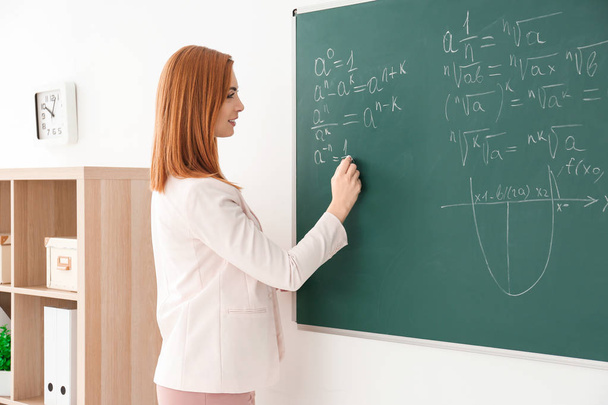 Beautiful young teacher writing on blackboard in classroom - Фото, изображение