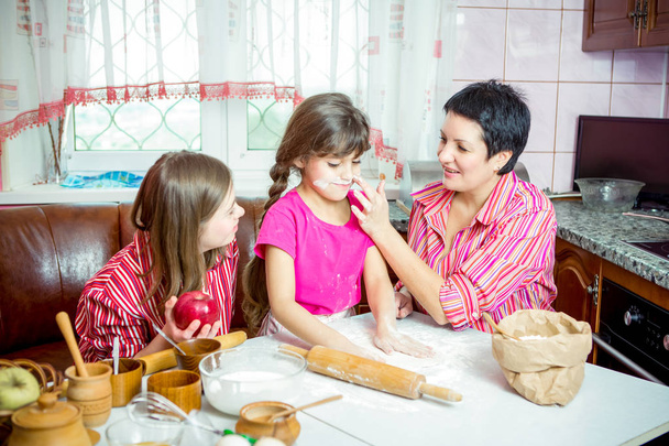 Moeder onderwijs van haar twee dochters koken op de keuken. - Foto, afbeelding