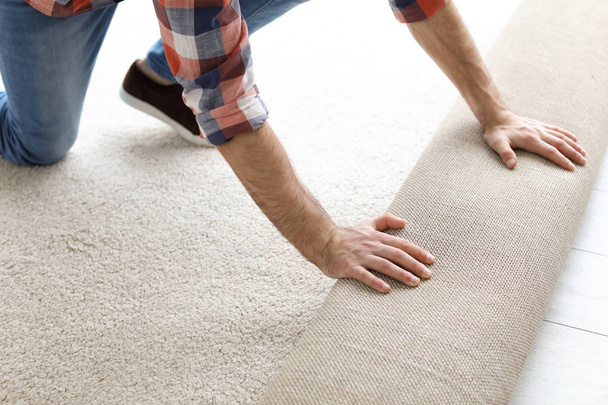 Man rolling out new carpet flooring in room - Фото, изображение
