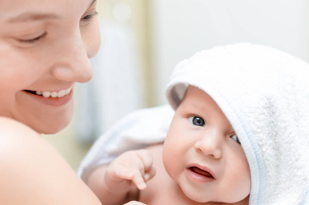Matka hospodářství kojenecká baby po koupání. Roztomilé dítě v bílý ručník na ruce maminky poté koupel. Děti koncept péče a hygiena - Fotografie, Obrázek
