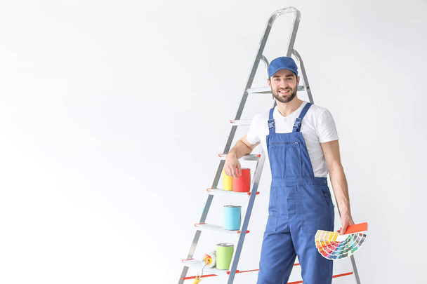 Male decorator with color palette near ladder on white background - Фото, зображення