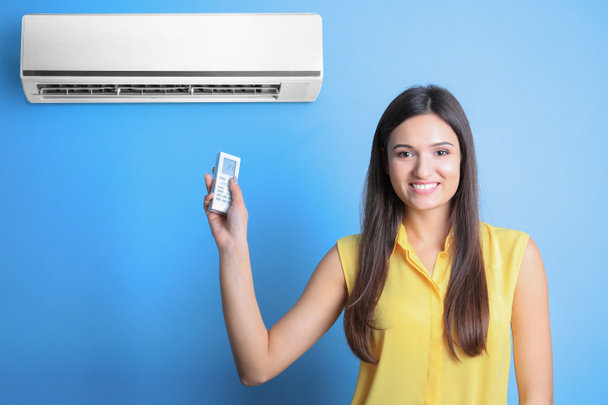 junge Frau schaltet Klimaanlage vor farbigem Hintergrund ein - Foto, Bild