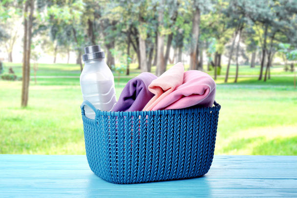Vaatteilla ja pyykinpesuaineella varustettu kori pöydällä ulkona
 - Valokuva, kuva