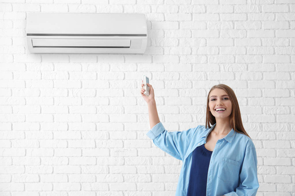 Jonge vrouw air conditioner tegen bakstenen muur achtergrond inschakelen - Foto, afbeelding
