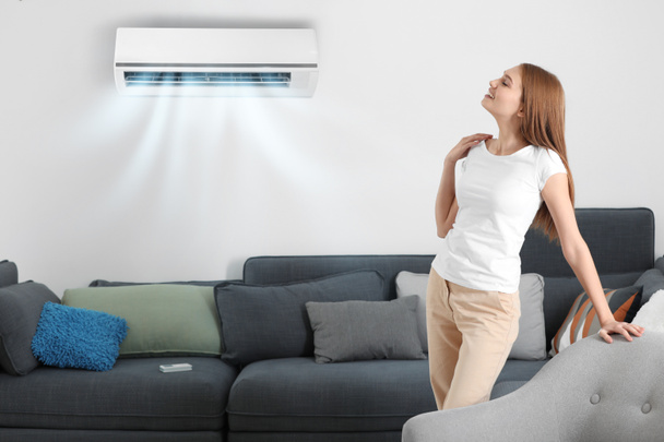 Jovem desfrutando de fluxo de ar fresco do condicionador em casa
 - Foto, Imagem