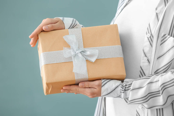 Woman holding gift box on color background, closeup - Photo, Image