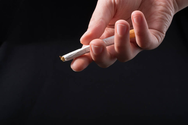 Hand verteilt Zigarette auf schwarzem Hintergrund - Foto, Bild
