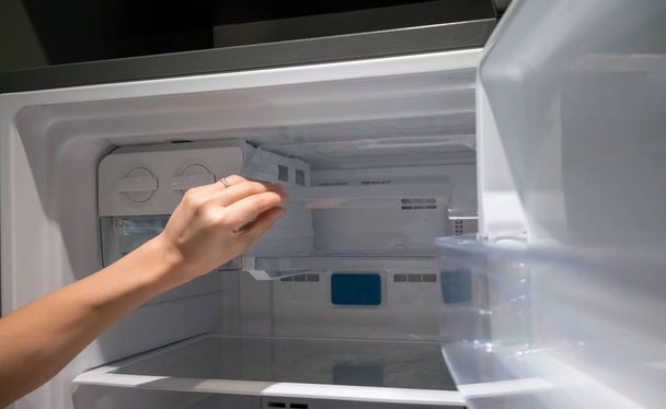 Nő kéz nyitott konténer átlátszó műanyag jég hűtőszekrényben. - Fotó, kép