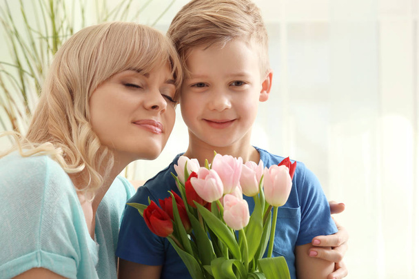Portrait of cute little boy and his mother with tulip bouquet at home - Photo, Image