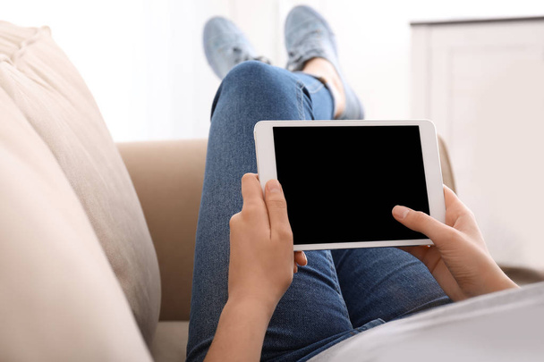 Jovem mulher usando computador tablet enquanto descansa no sofá em casa
 - Foto, Imagem