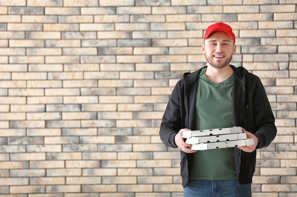 Young man with cardboard pizza boxes on brick wall background. Food delivery service - Foto, immagini