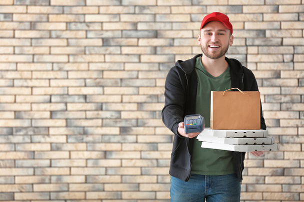 Jeune homme avec boîtes à pizza en carton, sac en papier et terminal bancaire sur fond de mur de briques. Service de livraison de nourriture
 - Photo, image
