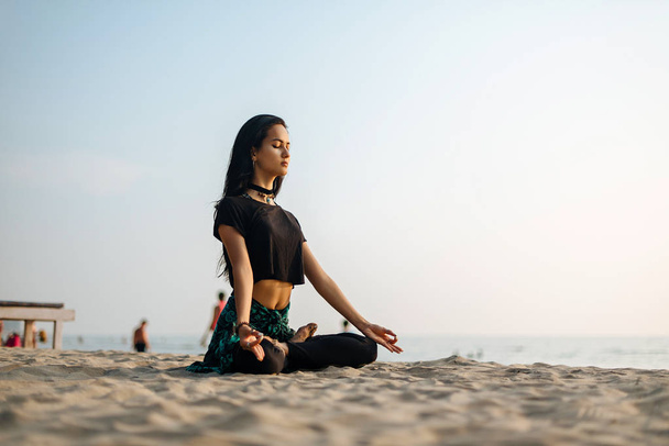 Young healthy woman practicing yoga on the beach at sunset - Фото, изображение