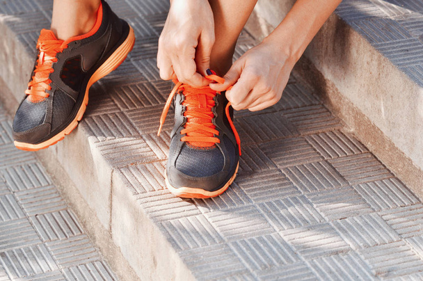 Woman tying laces of running shoes before training sitting on stairs - Φωτογραφία, εικόνα