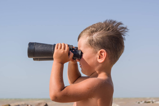 Gebruinde jongen met een verrekijker tegen de stormachtige zee - Foto, afbeelding
