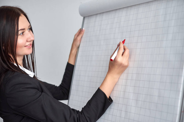 Beautiful smiling young woman writing on a blank flipchart in office as she does a presentation or promotion - Foto, immagini
