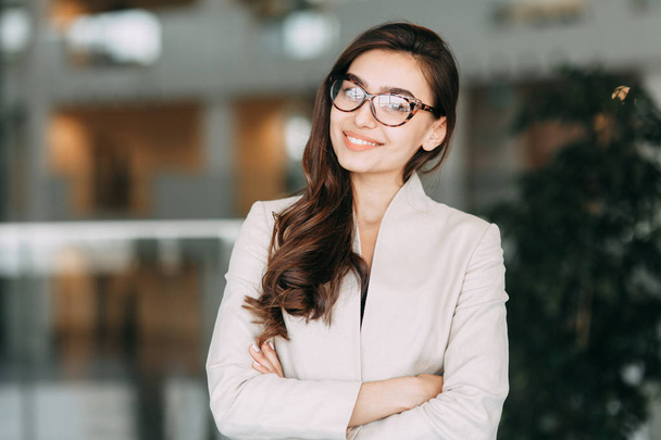 Mooie Russische bedrijf meisje met bril, permanent met gekruiste armen en lachend. Office-stijl en imago bedrijf, zakelijke bijeenkomst en groet - Foto, afbeelding
