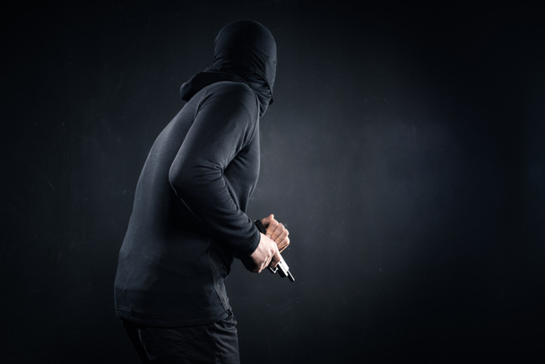 Robber with gun sneaking on black background - Fotografie, Obrázek