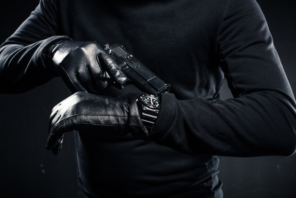 Mann mit Handschuhen und Pistole kontrolliert seine Uhr  - Foto, Bild