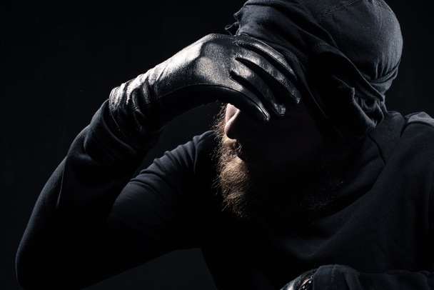  Robber in balaclava leaning his head on hand - Photo, Image