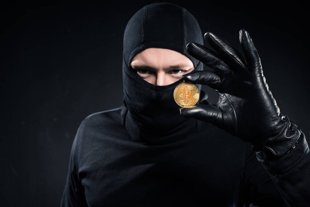 Man in black balaclava holding golden bitcoin - Fotoğraf, Görsel