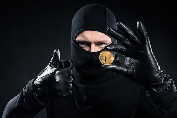 Man in black balaclava holding bitcoin and showing thumb up - Foto, imagen