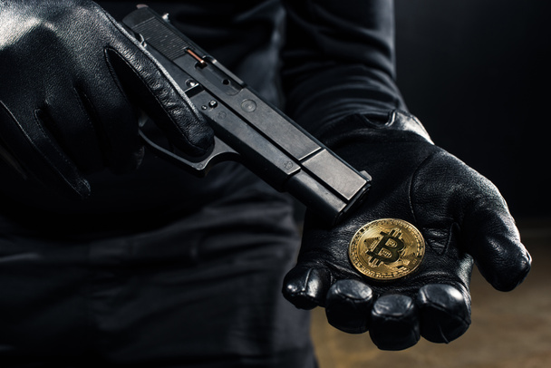 Vista de cerca de pistola y bitcoin en manos de ladrón
 - Foto, Imagen
