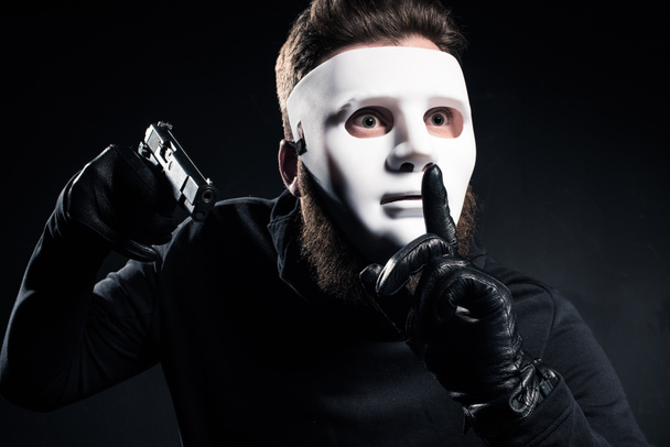 Räuber mit Maske hält Waffe in der Hand und zeigt Schweigegeste - Foto, Bild