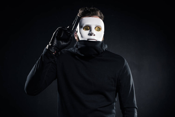 Thief in mask and bitcoins on eyes holding gun - Фото, изображение