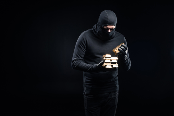 Ladrón en pasamontañas apilando lingotes de oro en sus manos
 - Foto, imagen