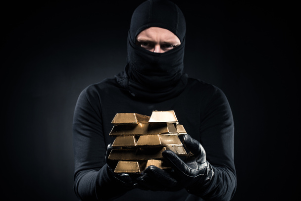 Man in balaclava bedrijf gouden bullions in zijn handen - Foto, afbeelding