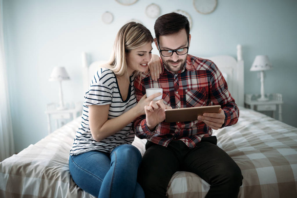 Young happy couple using digital tablet in bedroom - Фото, изображение