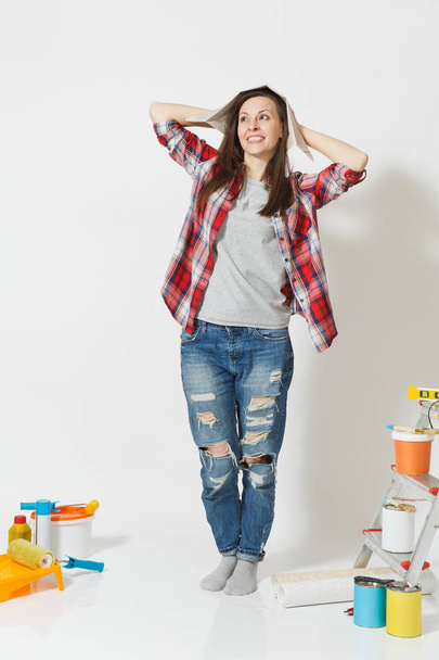 Täyspitkä muotokuva nainen sanomalehden hattu seisoo lähellä välineitä remontin asunnon eristetty valkoisella pohjalla. Taustakuva, tarvikkeet liimaamalla, maalaus työkaluja. Korjauskäsite
. - Valokuva, kuva