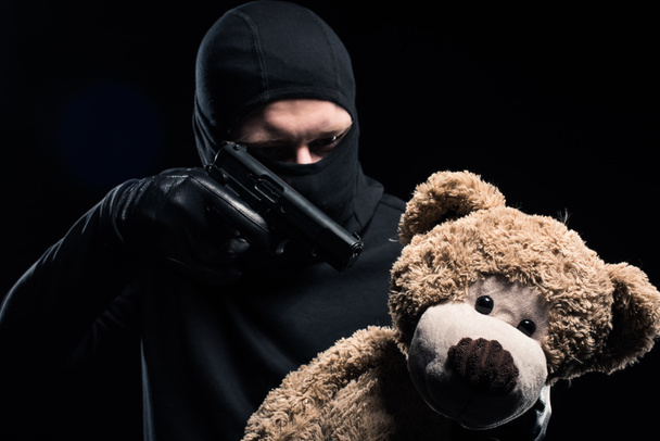 Robber in balaclava aiming at teddy bear - Photo, Image