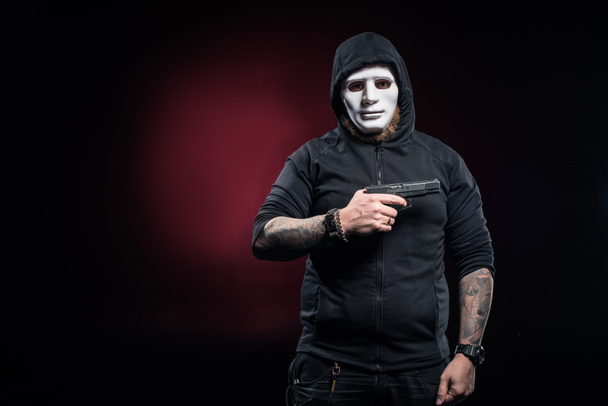 Robber in mask and balaclava holding gun - 写真・画像