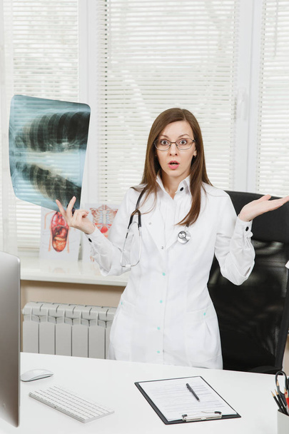 Jeune femme confiante médecin debout au bureau, tenant des rayons X des poumons, fluorographie, roentgen dans le bureau léger à l'hôpital. Femme en robe médicale, stéthoscope en salle de consultation. Concept de médecine
. - Photo, image