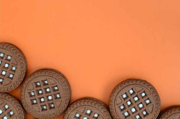 Detailed picture of dark brown round sandwich cookies with coconut filling on an orange surface. Background image of a close-up of several treats for tea - Photo, Image