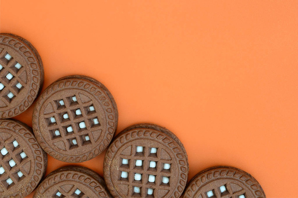 Λεπτομερή εικόνα της σκούρο καφέ στρογγυλά μπισκότα με καρύδα πλήρωση σε πορτοκαλί επιφάνεια. Εικόνα φόντου από μια στενή-up από τα πολλά κεράσματα για τσάι - Φωτογραφία, εικόνα