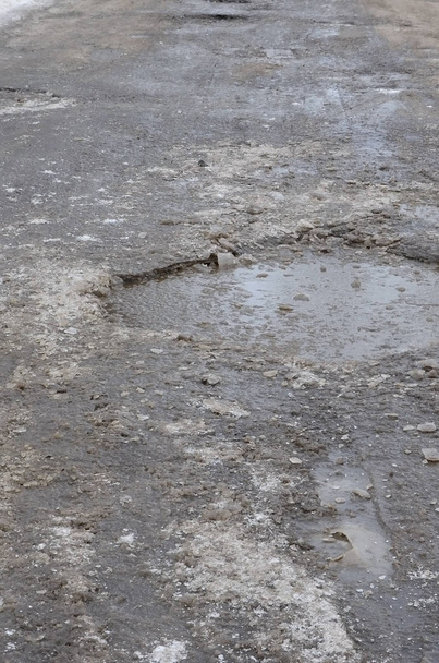 Uszkodzone drogi asfaltowej z jezdni spowodowane zamrażania i rozmrażania w okresie zimowym. Zły stan techniczny jezdni - Zdjęcie, obraz