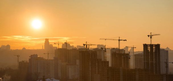 Панорама заката в городе с силуэтом зданий и промышленных кранов
 - Фото, изображение