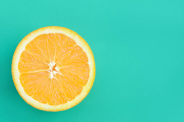 Widok z góry jeden plasterek pomarańczowy owoc na jasnym tle w turkus zielony kolor. Obraz nasycony tekstury owoców cytrusowych - Zdjęcie, obraz