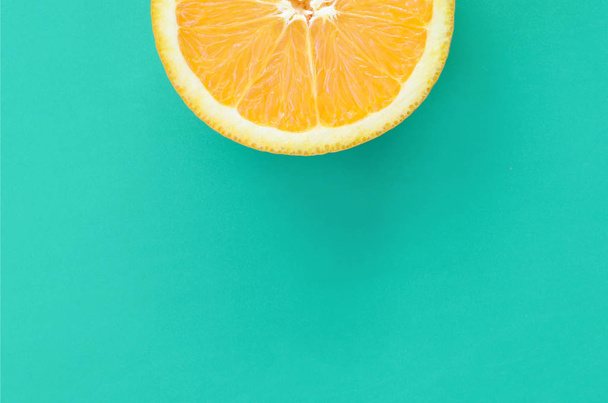 Top view of a one orange fruit slice on bright background in turquoise green color. A saturated citrus texture image - Photo, Image