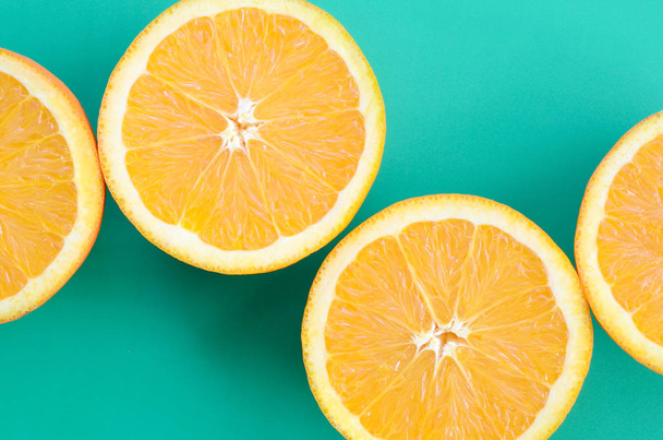 Top view of a several orange fruit slices on bright background in turquoise green color. A saturated citrus texture image - 写真・画像