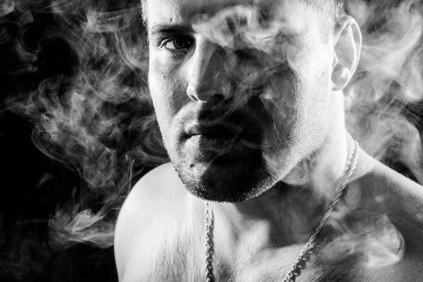 Mladý muž kouří vape a vydechuje bílý kouř na černém pozadí izolované - Fotografie, Obrázek